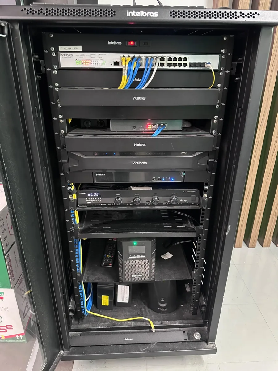 Interior de rack de CFTV com cabeamento organizado, switch PoE, gravador e nobreak.